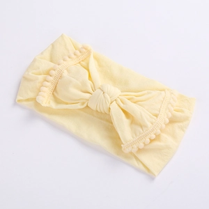 Close-up of soft cream yellow baby headband with pom-pom trim and central bow design