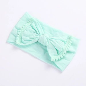 Detail of mint green baby headband featuring large bow and white pom-pom fringe trim