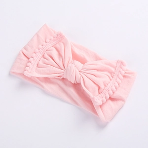 Detailed view of pink elastic baby headband with large bow and pom-pom lace trim edge