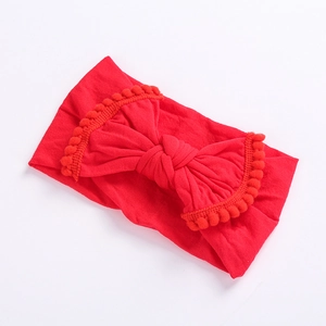Close-up of red elastic baby headband with large bow and decorative pom-pom fringe