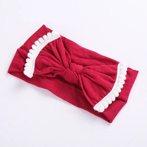 Close-up of red elastic baby headband with large bow and white pom-pom trim details