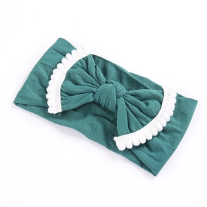 Detailed view of dark green baby nylon headband with pom-pom trimmed bow