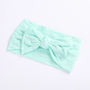 Macro detail of soft mint green nylon baby headband featuring a large bow on white surface