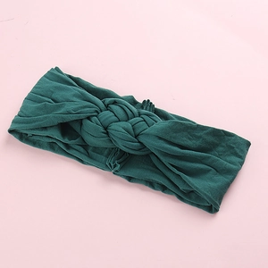 Détail d'un bandeau en tricot vert foncé pour bébé avec nœud tressé sur surface rose
