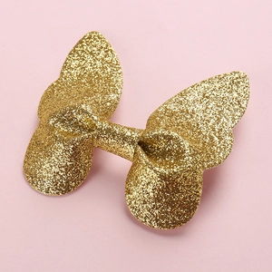 Close-up of golden glitter 3D butterfly hair clip on a soft pink background