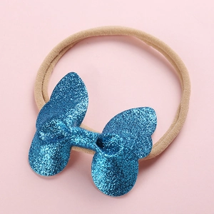 Détail d'un bandeau pour bébé avec ruban beige et un nœud bleu scintillant à paillettes