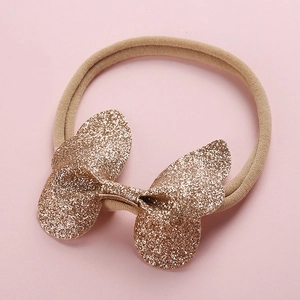 Détail d'un nœud papillon à paillettes dorées sur un bandeau élastique pour nouveau-nés