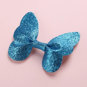 Detailed close-up of blue glitter 3D butterfly hair clip on a soft pink background