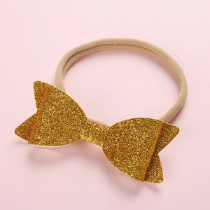 Close-up of baby headband featuring a large golden sequin bow on a soft nude nylon band