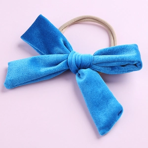 Détail d'un nœud en velours bleu sur un bandeau en nylon beige élastique pour bébé