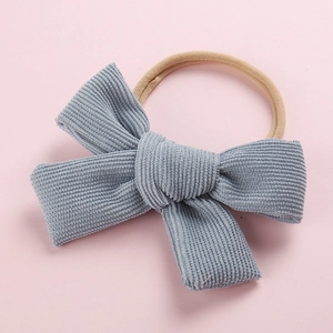 Vue détaillée du nœud en velours côtelé bleu-gris avec bandeau en nylon sur fond rose uni