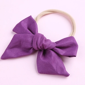 Détail d'un nœud en coton violet sur un bandeau en nylon beige pour bébé fille