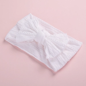 Close-up of white knitted baby headband with a cable stitch texture and large bow detail