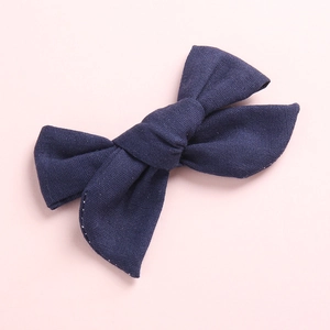 Gros plan d'une barrette nœud bleu marine en lin texturé sur une surface rose tendre