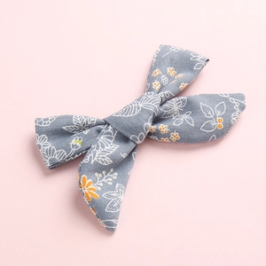 Grey floral fabric bow hair clip with white leaves and orange flowers on pink background