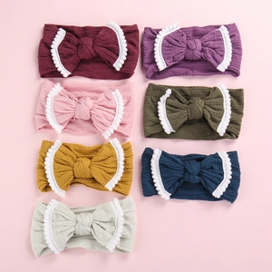 Vue à plat de sept bandeaux pour bébés en tricot torsadé avec nœuds et bords à pompons