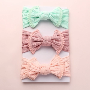 Détail de trois bandeaux bébé en jacquard avec bords pompons et grands nœuds tricotés