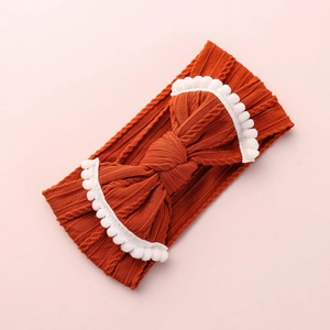 Détail du bandeau orange pour bébé avec nœud et bordure de pompons blancs