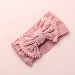 Détail du bandeau jacquard rose pour bébé avec un grand nœud et des pompons mignons