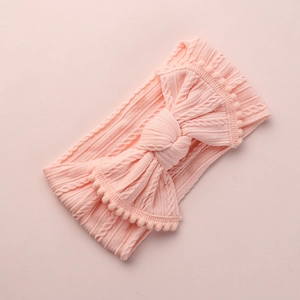 Vue détaillée du bandeau bébé en tricot torsadé avec grand nœud et bordure à pompons