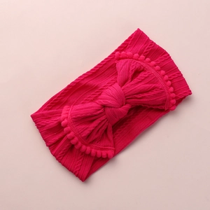Détail d'un bandeau en tricot rose pour bébé avec nœud géant et bordure à pompons