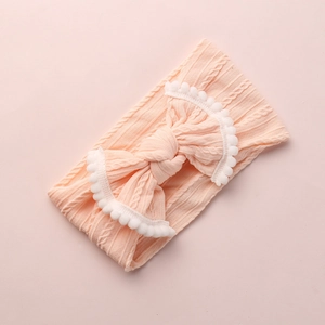 Détail du bandeau tricoté rose pour bébé avec gros nœud et bordure pompon blanc