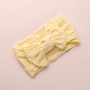 Détail d'un bandeau bébé jaune clair avec nœud jacquard et bordure à pompons