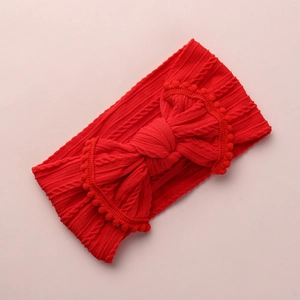 Détail du bandeau bébé en maille rouge avec grand nœud et bordure à pompons doux