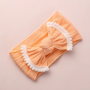 Détail du bandeau bébé en maille torsadée rose-orange avec nœud en dentelle pompon