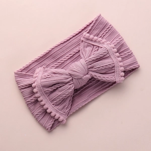 Détail du bandeau bébé tricoté rose poudré avec grand nœud à pompons décoratifs