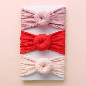 Detailed view of three ribbed knit baby headbands in pink, red, and cream with donut knots