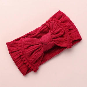 Détail du bandeau bébé tricoté rouge foncé avec nœud et bordure en pompons doux