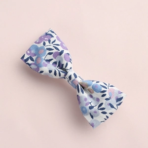 Détail d'une pince à cheveux nœud en coton fleuri avec fleurs violettes sur fond rose