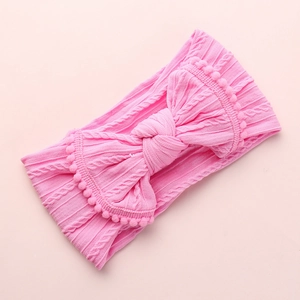 Texture tricotée détaillée d'un bandeau rose pour bébé avec nœud et pompons