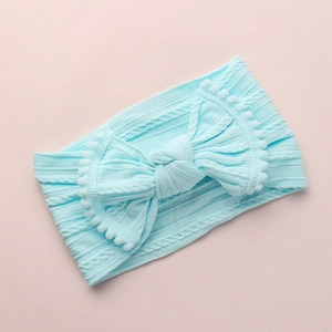 Détail du bandeau bébé bleu clair avec texture tricotée douce et grand nœud à pompons