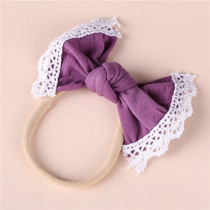 Close-up of baby headband with purple knit bow and white lace trim on pink background