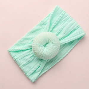 Detail view of mint green jacquard knit baby headband with donut knot on pink background