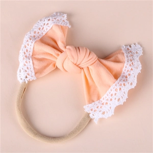Detail of baby headband featuring peach bow with white lace trim on nude nylon band