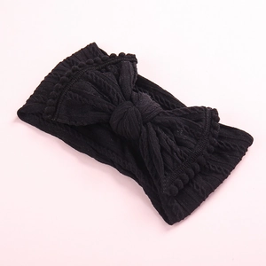 Détail du bandeau bébé en maille noire avec un grand nœud et des bords à pompons décoratifs