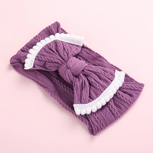 Détail d'un bandeau en tricot violet pour bébé avec grand nœud et bordure de pompons