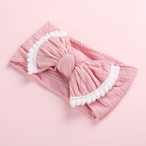 Gros plan détaillé d'un bandeau tricoté rose pour bébé avec pompons et grand nœud