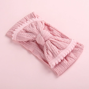 Détail du bandeau en tricot rose pour bébé avec gros nœud et bordure à pompons doux