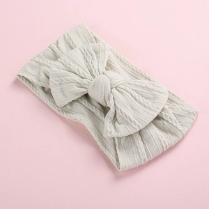 Detail of soft cream knitted baby headband with a large bow and cable knit texture