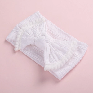Détail macro du bandeau bébé blanc en tricot torsadé avec un nœud et des pompons