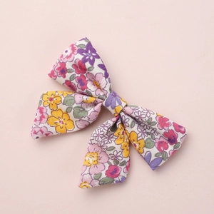 Floral print baby bow hair clip with yellow and pink blossoms on a soft pink background