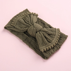 Détail du bandeau bébé en maille vert olive avec grand nœud et bordure à pompons