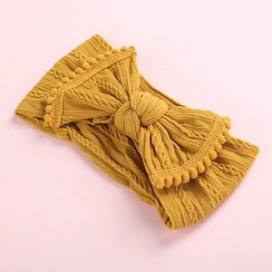 Détail du bandeau tricoté pour bébé jaune gingembre avec grand nœud à pompons et maille torsadée
