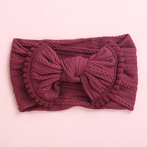 Détail du bandeau bébé en tricot torsadé bordeaux avec nœud et petits pompons