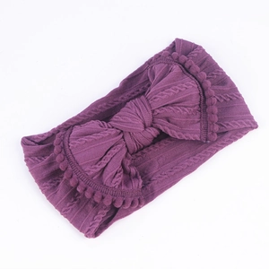 Bandeau bébé violet en maille douce avec un grand nœud et des pompons sur fond blanc