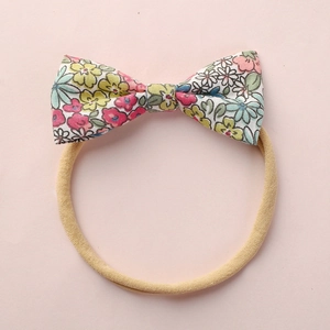 Détail d'un bandeau bébé avec nœud à fleurs et sangle élastique en nylon nude